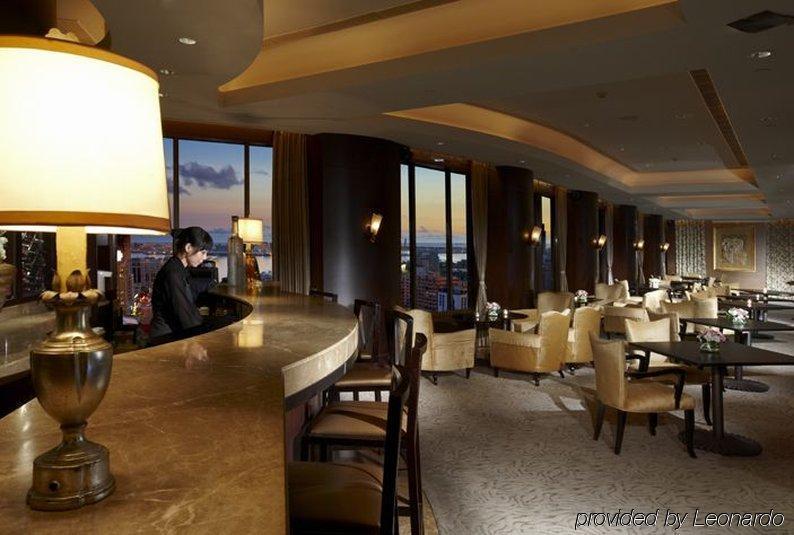 Ambassador Hotel Καοσιούνγκ Εστιατόριο φωτογραφία The photo depicts an elegant bar or lounge area within a high-rise setting. The interior features warm lighting, with a large lamp illuminating the bar counter. There is a bartender seated at the bar, and the space includes plush chairs and tables ar
