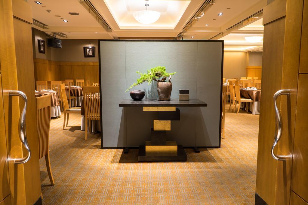 Ambassador Hotel Καοσιούνγκ Εξωτερικό φωτογραφία The photo shows the interior of a restaurant. In the foreground, there is a decorative table with a minimalist design, featuring a vase with greenery. The background reveals a spacious dining area with wooden chairs and tables, creating a warm and in