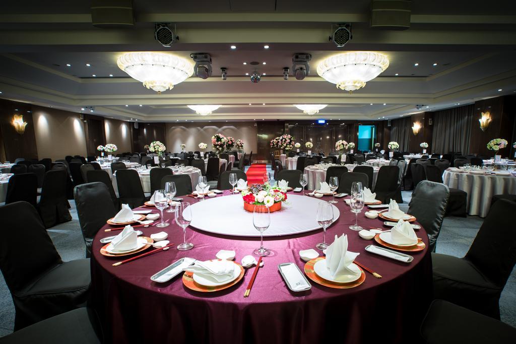 Ambassador Hotel Καοσιούνγκ Εξωτερικό φωτογραφία The photo depicts an elegantly set dining area for an event. 

In the foreground, there is a circular table covered with a dark red tablecloth, featuring a centerpiece of flowers in vibrant colors. The table is equipped with white plates, polished cu