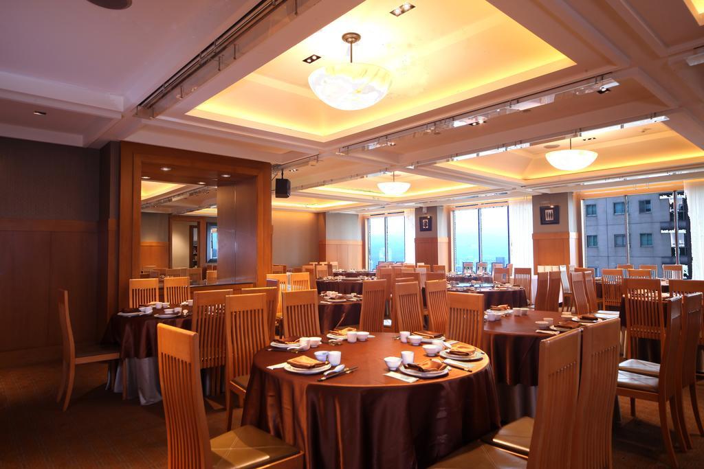 Ambassador Hotel Καοσιούνγκ Εξωτερικό φωτογραφία The photo shows the interior of a restaurant. It features several round tables covered with brown tablecloths, each set with plates and utensils. The room is well-lit with overhead lighting, and large windows allow natural light to enter, providing a