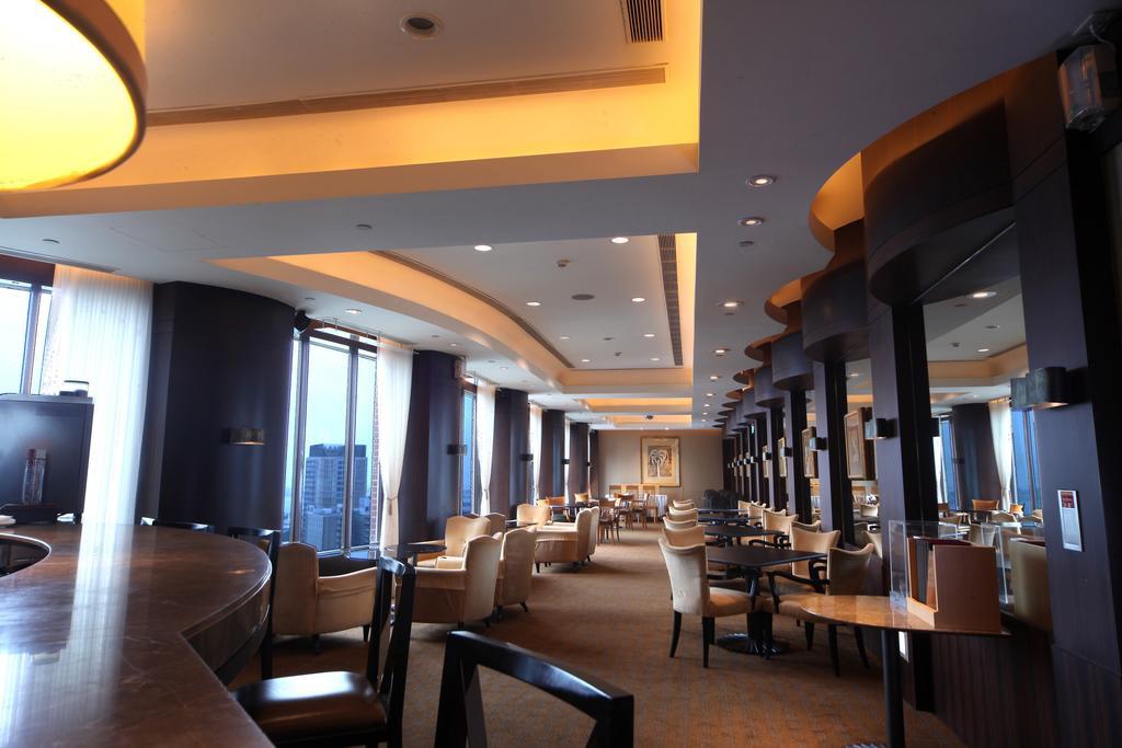 Ambassador Hotel Καοσιούνγκ Εξωτερικό φωτογραφία The photo shows the interior of a modern restaurant or lounge. The space features elegant seating with cream-colored chairs and wooden tables, arranged in a spacious layout. Soft, warm lighting highlights the architectural details of the ceiling and 
