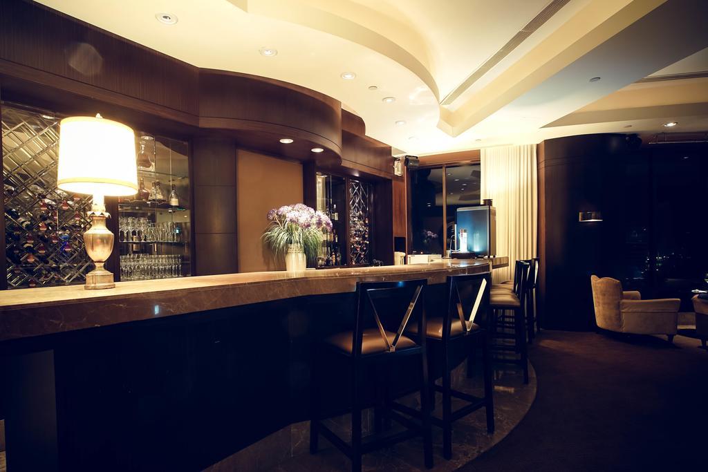 Ambassador Hotel Καοσιούνγκ Εξωτερικό φωτογραφία The photo shows a modern and stylish bar area. The bar is made of a smooth stone surface and features a backlit shelf displaying various bottles of liquor. There is a lamp on the bar providing warm lighting, and a vase with flowers adds a decorative 