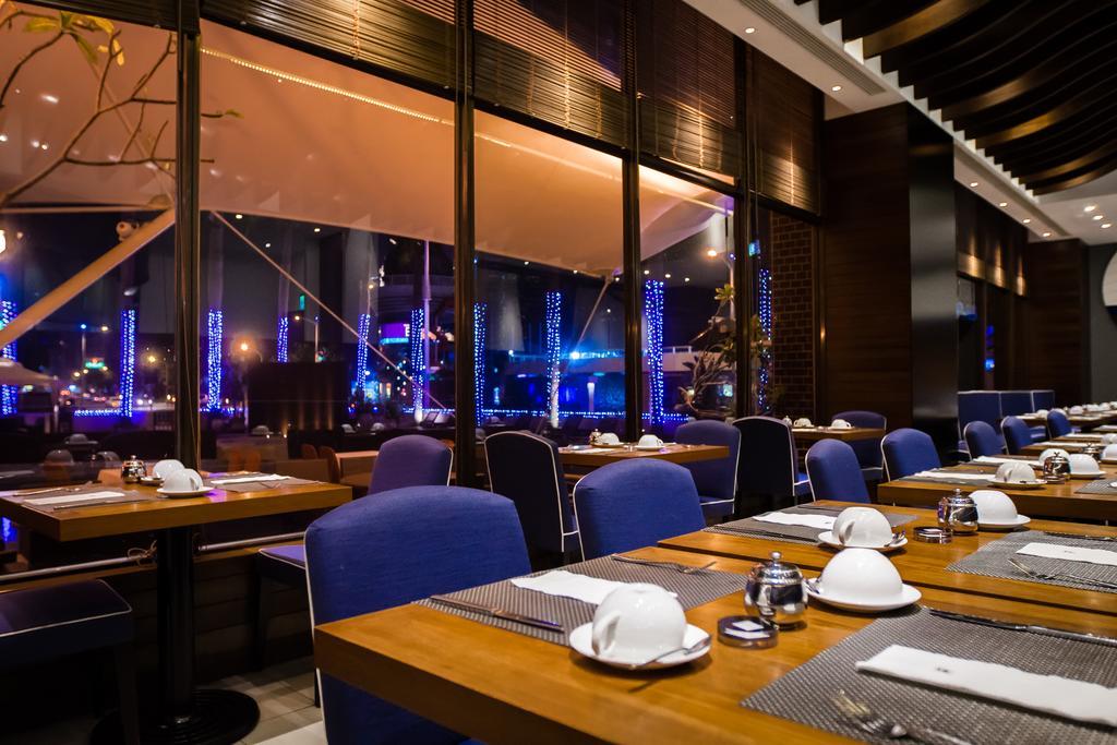 Ambassador Hotel Καοσιούνγκ Εξωτερικό φωτογραφία The photo shows the interior of a restaurant with a modern and elegant design. There are several tables set with white dishware and utensils, featuring a combination of dark wooden and blue upholstered seating. Large windows provide a view of a night