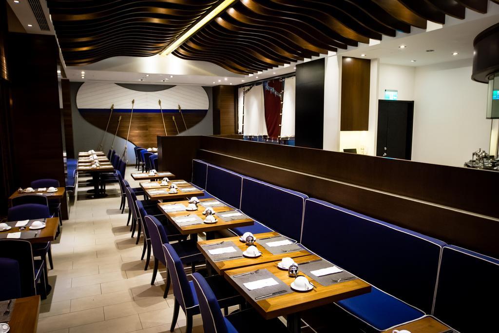 Ambassador Hotel Καοσιούνγκ Εξωτερικό φωτογραφία The photo shows the interior of a modern restaurant. The design features a combination of wooden and blue elements, with sleek lines and a stylish ceiling design. There are several tables set up, each with white plates and utensils. The seating inclu