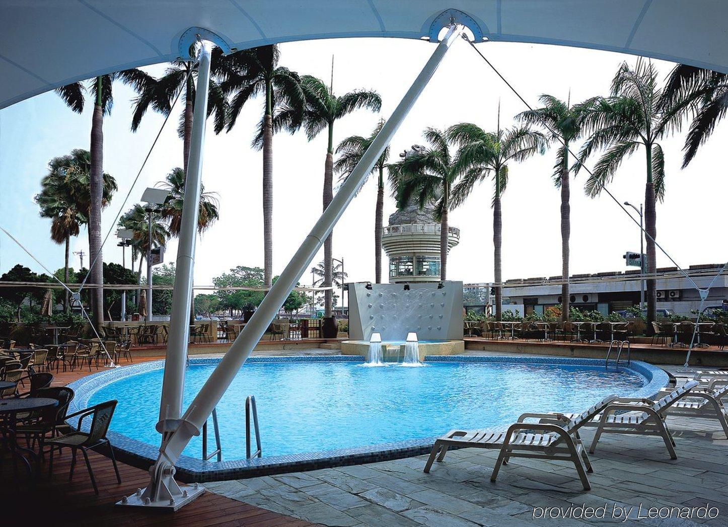 Ambassador Hotel Καοσιούνγκ Εξωτερικό φωτογραφία The photo shows a swimming pool area surrounded by tall palm trees. The pool has a clear blue water and features a waterfall-like structure. There are lounge chairs positioned around the pool, suggesting a relaxing atmosphere. A covered area provides