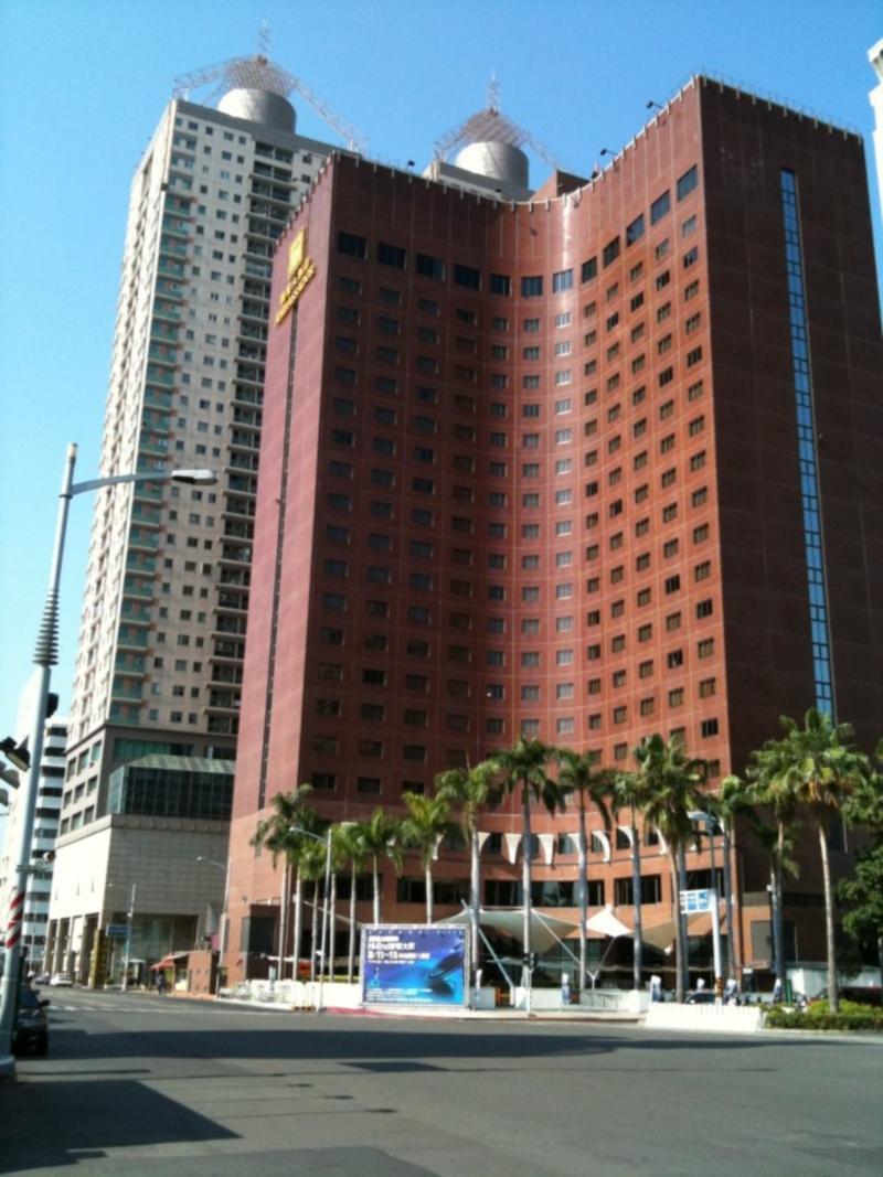 Ambassador Hotel Καοσιούνγκ Εξωτερικό φωτογραφία The photo shows a tall building made of red brick with many windows. It has a curved shape and is likely a hotel or office building. In front of the building, there are palm trees, suggesting a warm climate. To the left, there appears to be another t