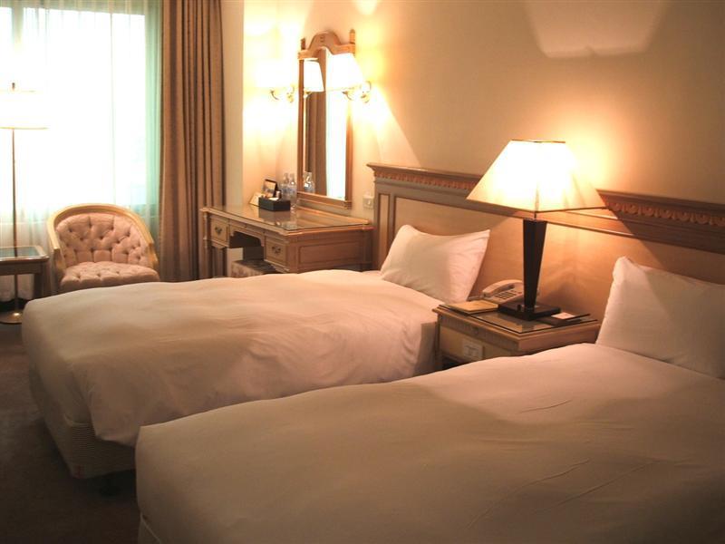 Ambassador Hotel Καοσιούνγκ Εξωτερικό φωτογραφία The photo shows a cozy hotel room with two single beds, each covered with white bedding. There is a lamp on a nightstand between the beds. A wooden dresser with a mirror is against the wall, and a comfortable armchair is placed nearby. Soft lighting 