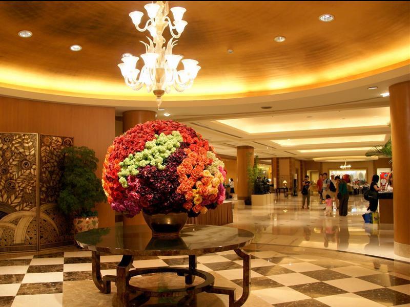 Ambassador Hotel Καοσιούνγκ Εξωτερικό φωτογραφία The photo shows the interior of a spacious lobby area, characterized by elegant design elements. In the center, there is a large round floral arrangement made up of vibrant flowers in various colors, displayed in a decorative vase on a dark, round ta