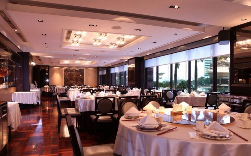 Ambassador Hotel Καοσιούνγκ Εξωτερικό φωτογραφία The photo shows an elegant dining room with a modern and upscale design. The space features round tables covered with white tablecloths, each set with neatly arranged dinnerware, including folded napkins. The floor is made of polished wood, enhancing
