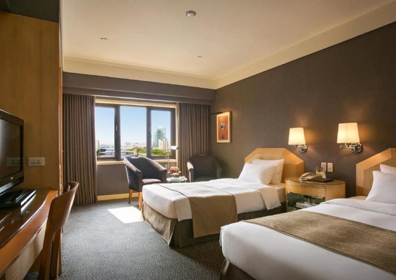 Ambassador Hotel Καοσιούνγκ Εξωτερικό φωτογραφία The photo shows a hotel room featuring two twin beds with beige and brown bedding. The room has a modern design with a dark accent wall and light-colored furniture. There are bedside lamps on each side of the beds, and a comfortable armchair is posit