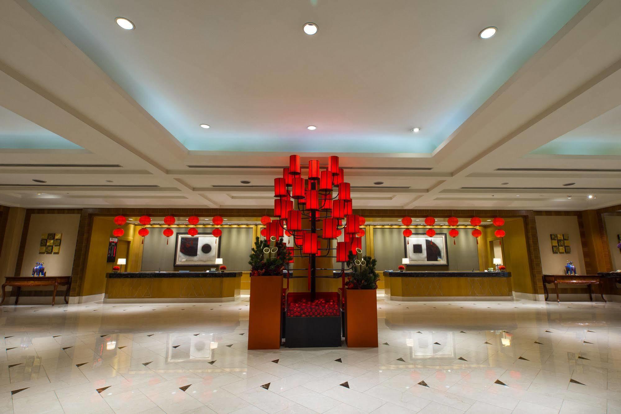 Ambassador Hotel Καοσιούνγκ Εξωτερικό φωτογραφία The photo depicts the interior of a hotel lobby. The area is well-lit and features elegant design elements. In the center, there is a striking installation of red lanterns, which adds a festive touch to the space. The lobby has a polished marble floo
