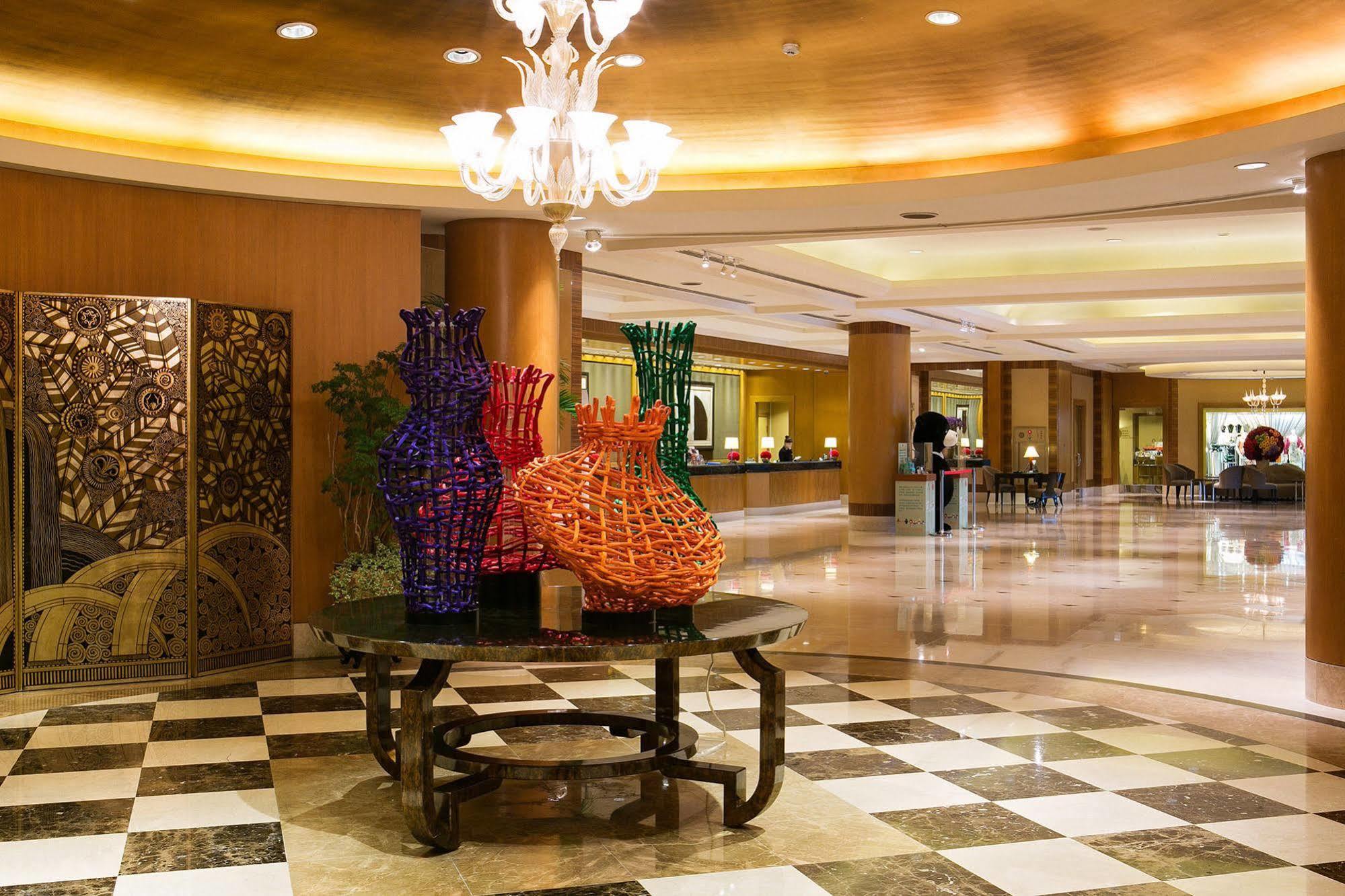 Ambassador Hotel Καοσιούνγκ Εξωτερικό φωτογραφία The photo shows the interior of a hotel lobby featuring an elegantly designed space. In the foreground, there is a decorative table with colorful woven vases, predominantly in purple and orange. These vases add a vibrant touch to the setting. The flo