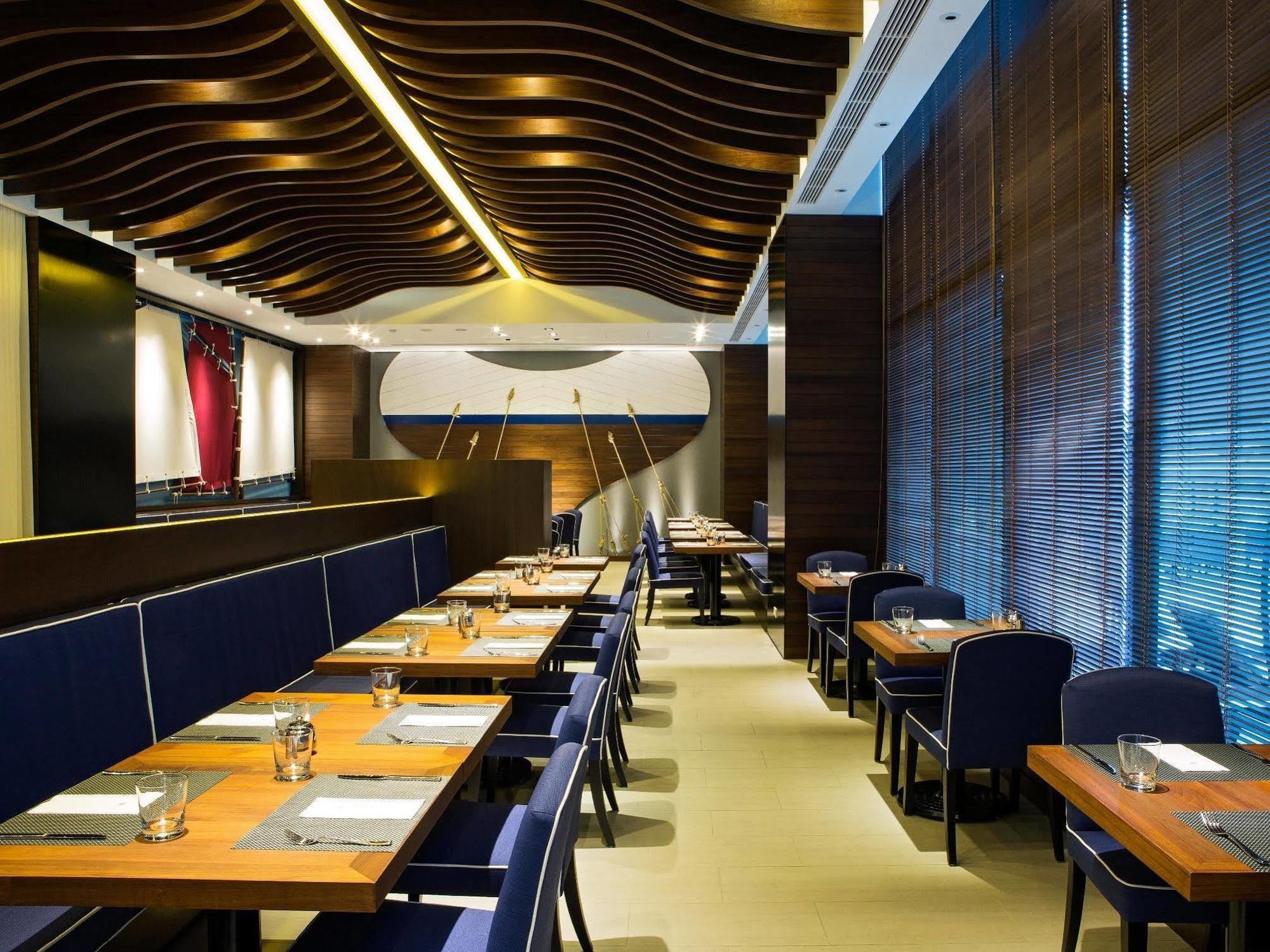 Ambassador Hotel Καοσιούνγκ Εξωτερικό φωτογραφία The photo shows the interior of a modern restaurant. It features wooden flooring and stylish seating arrangements with tables. The tables are set with menus, cutlery, and glasses, indicating a dining setup. The walls are adorned with contemporary des