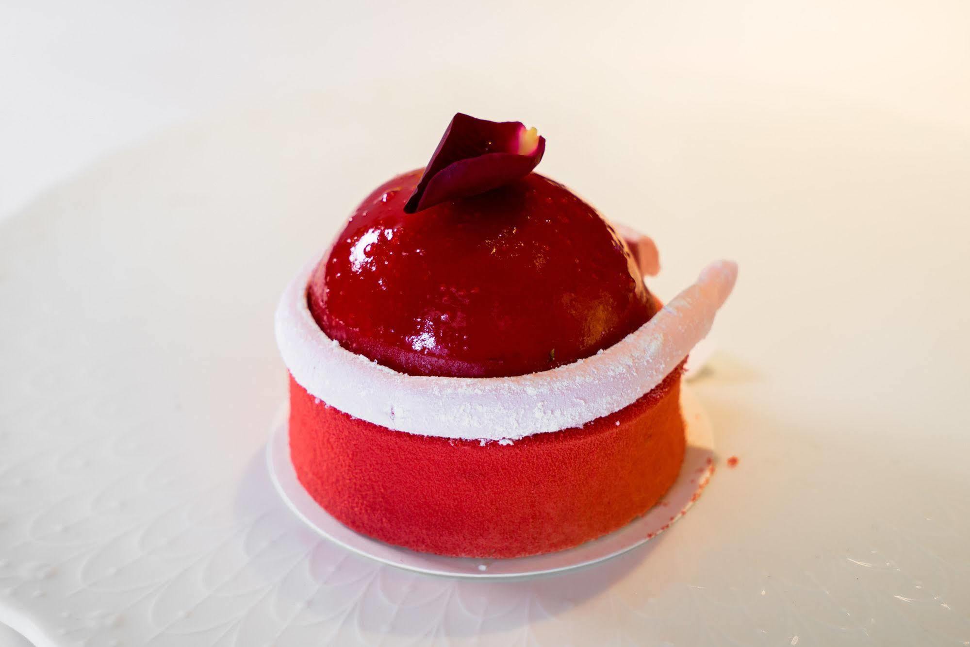 Ambassador Hotel Καοσιούνγκ Εξωτερικό φωτογραφία The photo shows a beautifully crafted dessert that appears to be a mousse or cake. It has a glossy red coating, shaped like a dome on top, with a small decorative rose petal placed on it. The base of the dessert features a gradient of colors, transit