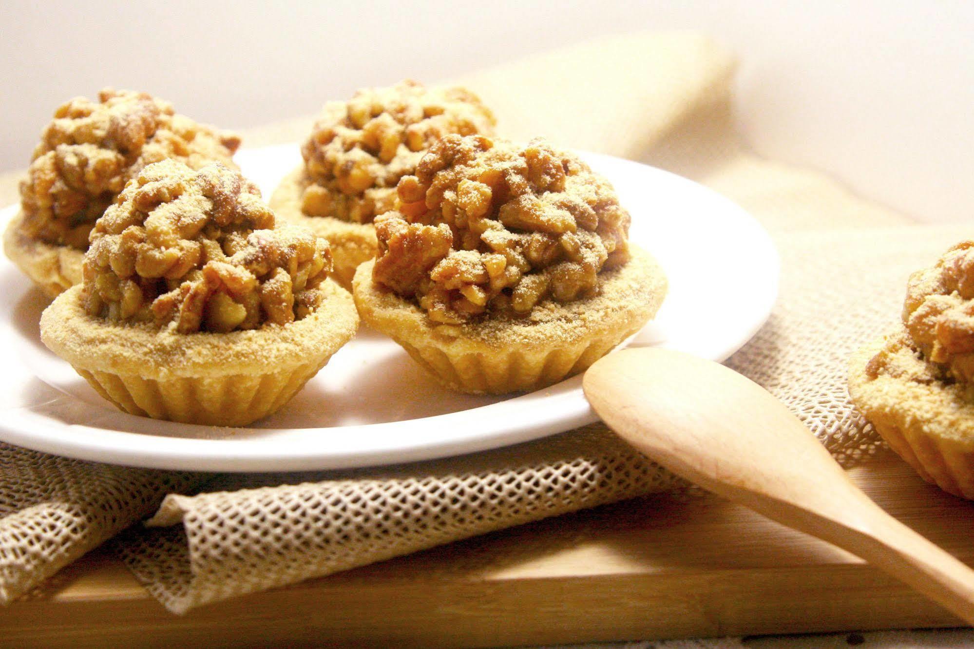 Ambassador Hotel Καοσιούνγκ Εξωτερικό φωτογραφία The photo shows a plate with small, dessert-like tarts. Each tart features a golden, crumbly crust that is filled with a mixture of chopped nuts and a sweet topping, likely caramelized for added flavor. The tarts are arranged neatly on a white plate,