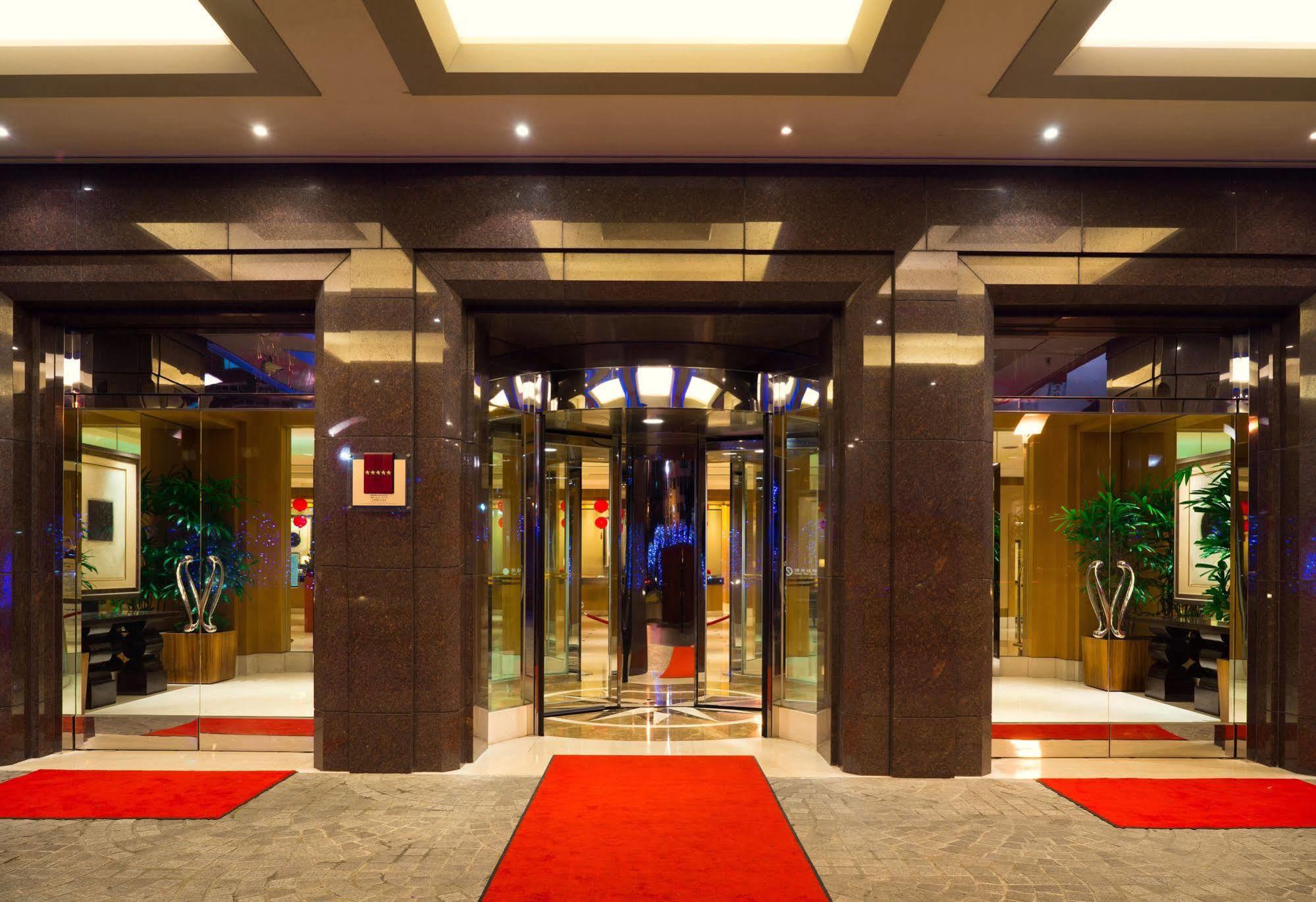 Ambassador Hotel Καοσιούνγκ Εξωτερικό φωτογραφία The photo shows the entrance of a modern hotel or building. It features large glass doors in a sleek frame, creating an inviting entrance. The floor is covered with a plush red carpet leading up to the doors. Inside, there are decorative plants on ei