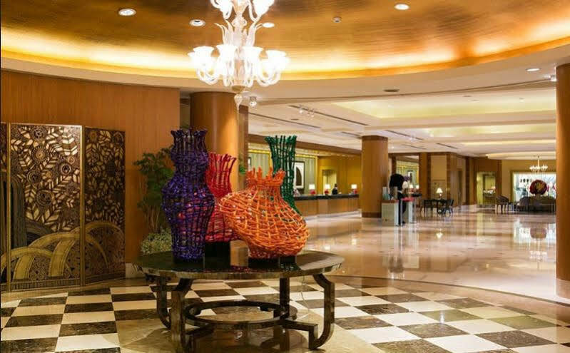 Ambassador Hotel Καοσιούνγκ Εξωτερικό φωτογραφία The image shows a spacious and elegantly designed lobby area. In the center, there are several large, artistic vases made of colorful materials, including shades of purple, orange, and green. These vases are displayed on a black table, contrasting wi